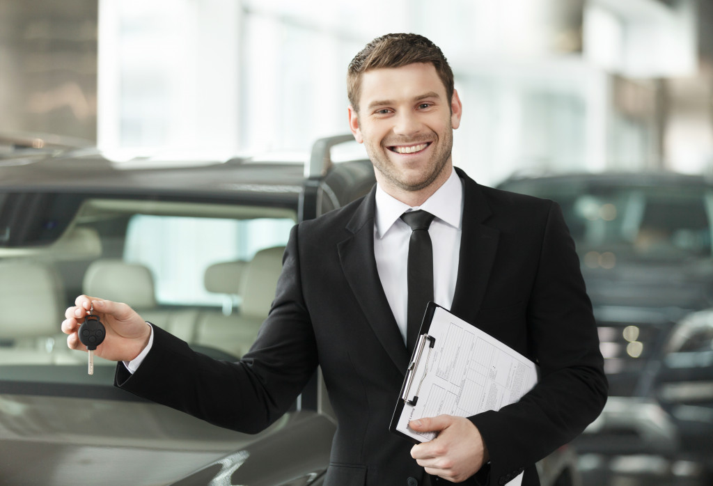 male car dealer smiling while holding car key in the dealership