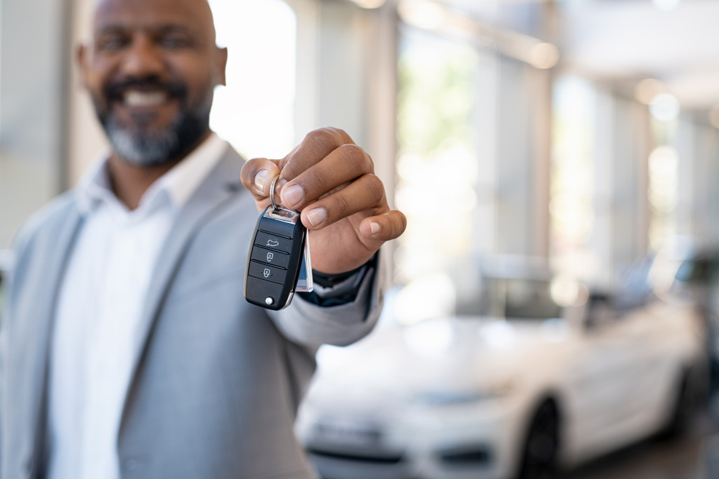 man smiling while holding car keys with cars in the background