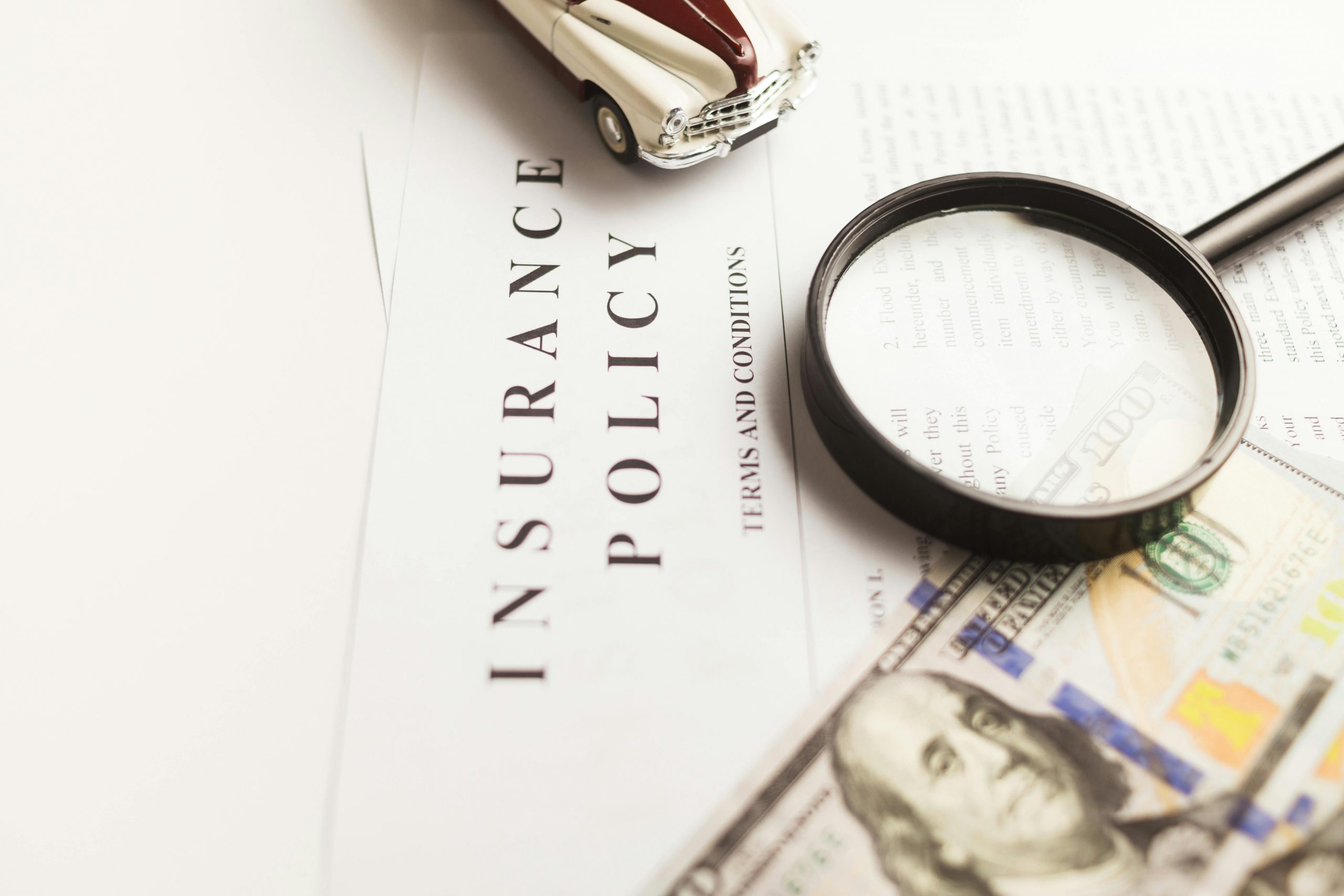 dollar bill, magnifying glass, and a miniature classic car on an insurance policy document