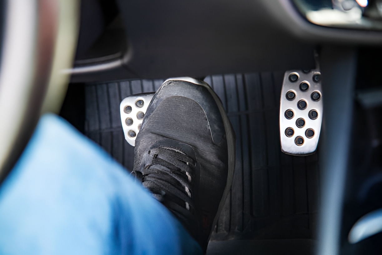 close-up of a foot in a black sneaker pressing a brake pedal